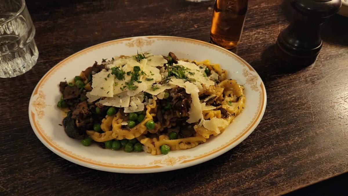A plate of vegetarian pasta freshly cooked with mushrooms and peas, in a beautiful beige plate on a wooden table with mood lighting.