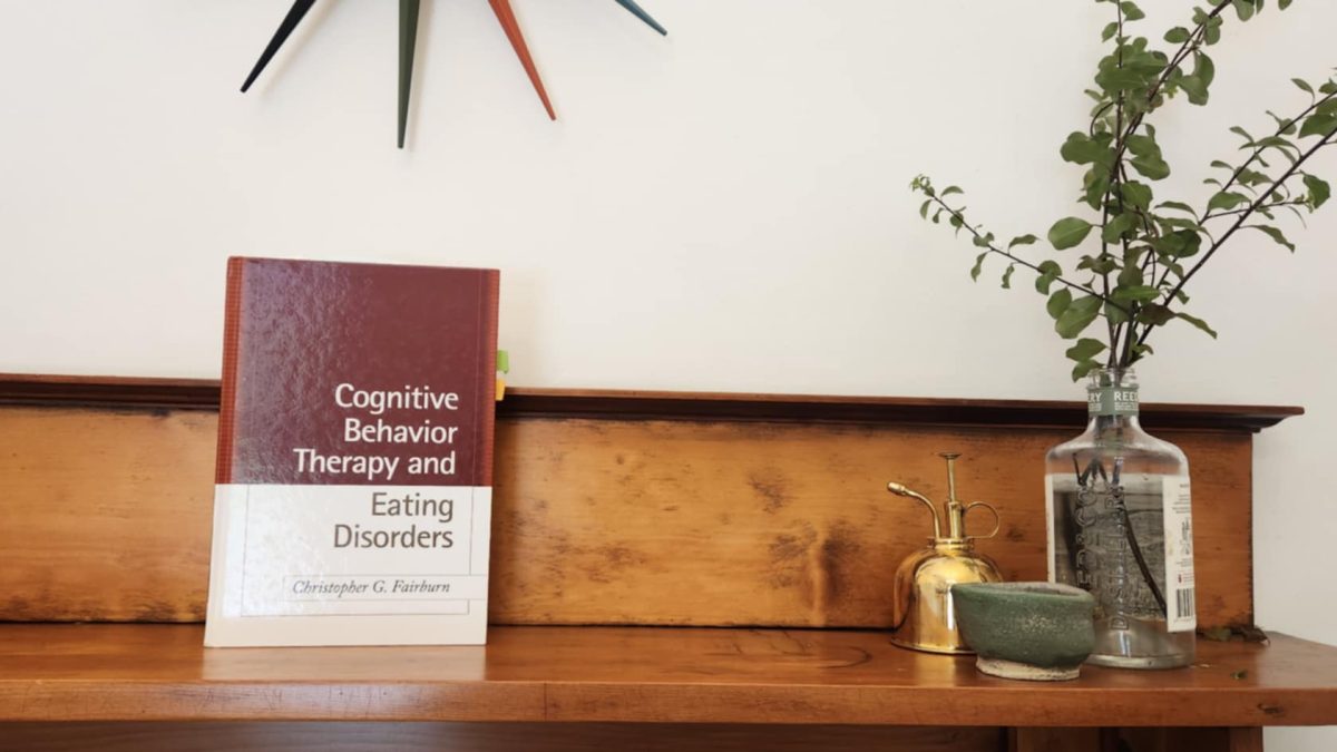 CBT-E book on a shelf, representing cognitive behavioral therapy for eating disorders and body image issues, a key resource in evidence-based treatment.